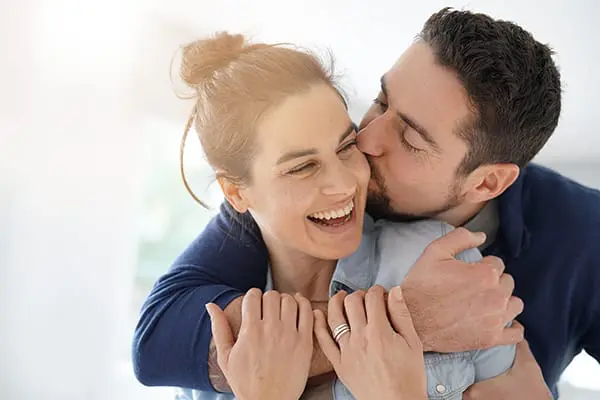 Frau und Mann halten sich lachend im Arm: Das Paar spricht offen über das Thema Genitalherpes.